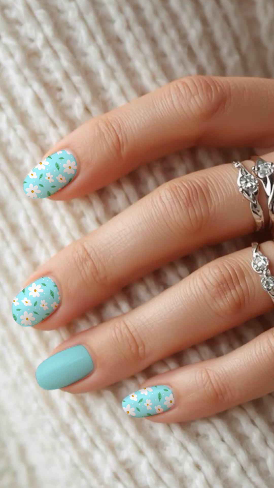 Hand with nails featuring a white daisy floral designs on a turquoise blue background.